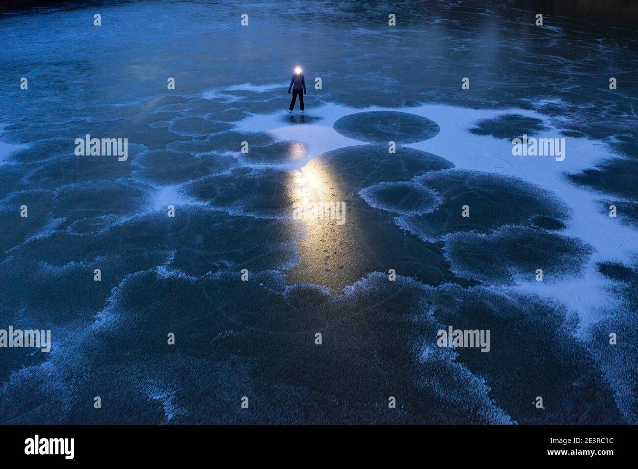 Donna con faro in piedi sul lago ghiacciato al crepuscolo Foto Stock