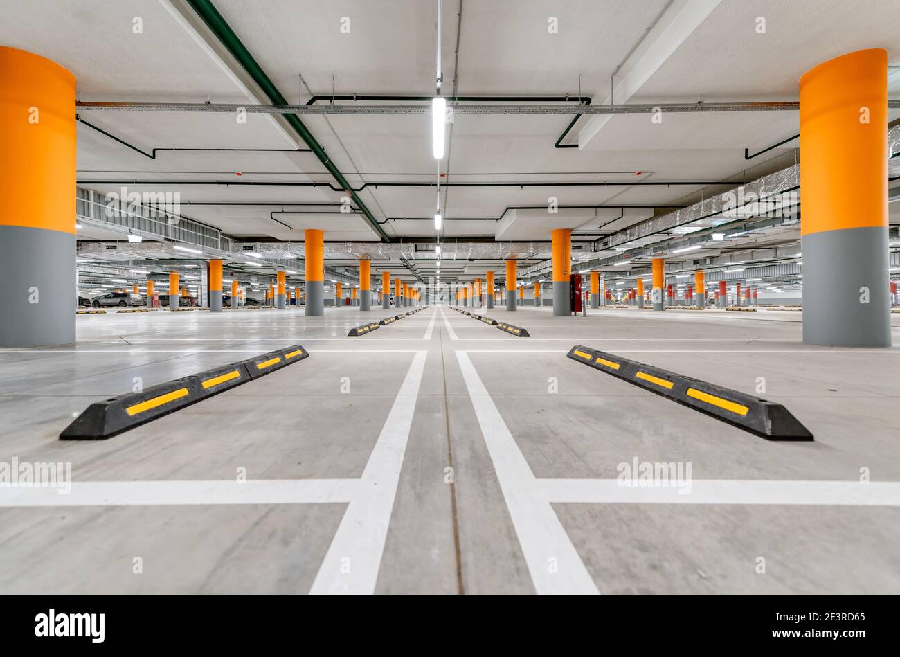 Ampio parcheggio sotterraneo per auto. Nuovo parcheggio vuoto con illuminazione luminosa. Le colonne sono dipinte di rosso e arancione. Foto Stock