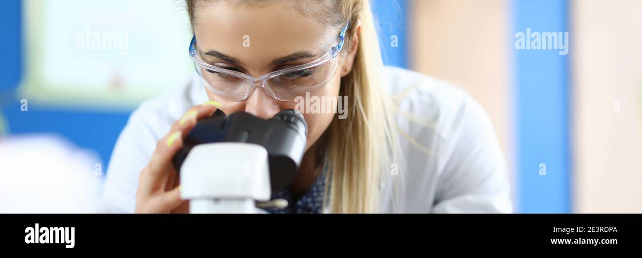 Donna a in laboratorio guarda attraverso il microscopio Foto Stock