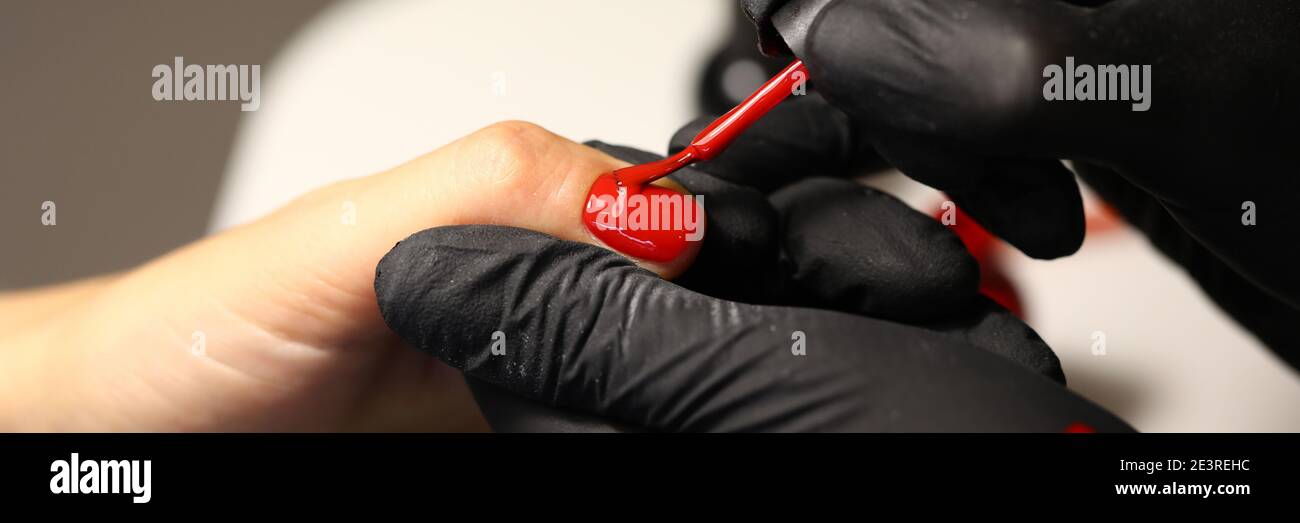 Mani in guanti neri applicare vernice rossa Foto Stock