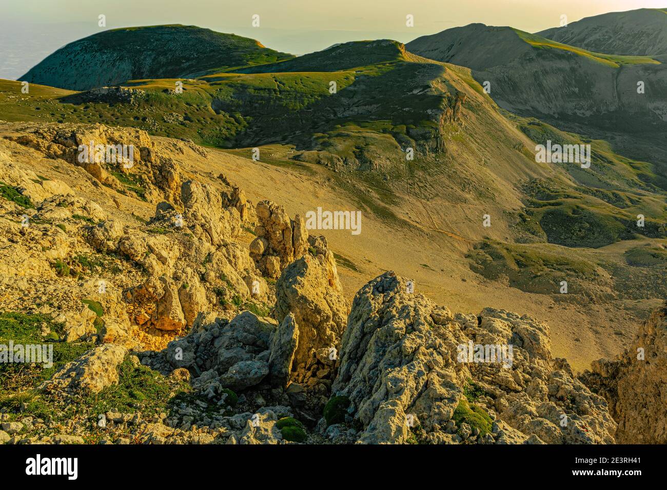 Rocce che si affacciano sulla valle della Cannella illuminate dalla prima luce dell'alba. Sullo sfondo la cima delle tre Portoni. Parco Nazionale della Maiella Foto Stock