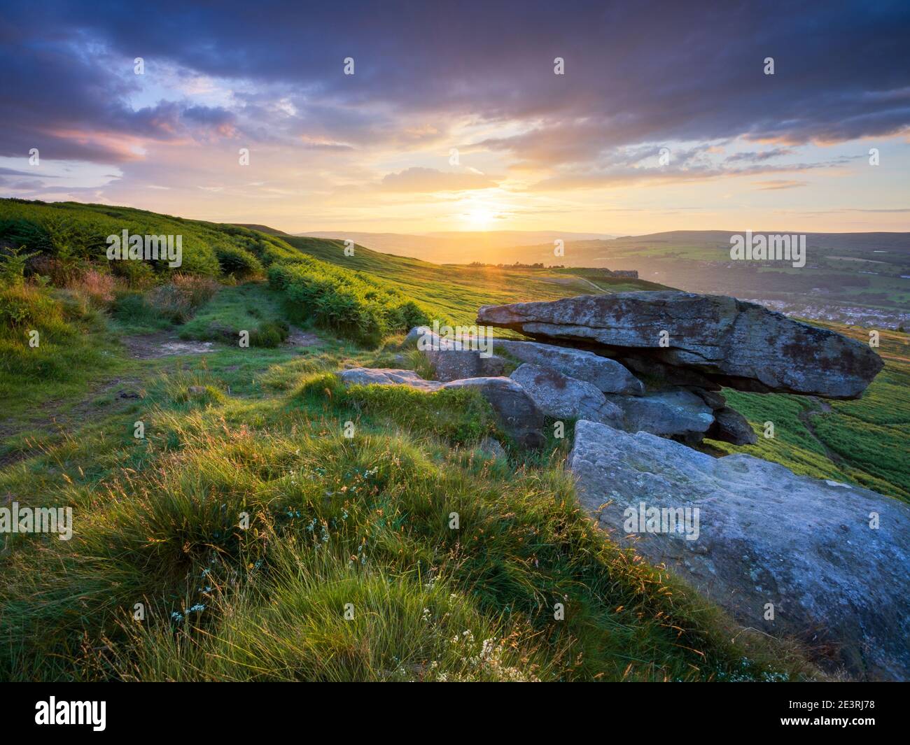 Il sole tramontante cade sotto una riva di nuvole e bagna il paesaggio che circonda Pancake Rock sul bordo di Ilkley Moor in luce dorata. Foto Stock
