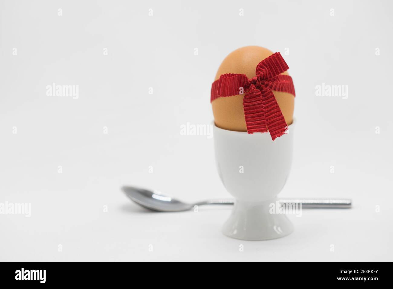 L'uovo bollito in coppe d'uovo con un cucchiaio e un nastro decorativo rosso Foto Stock