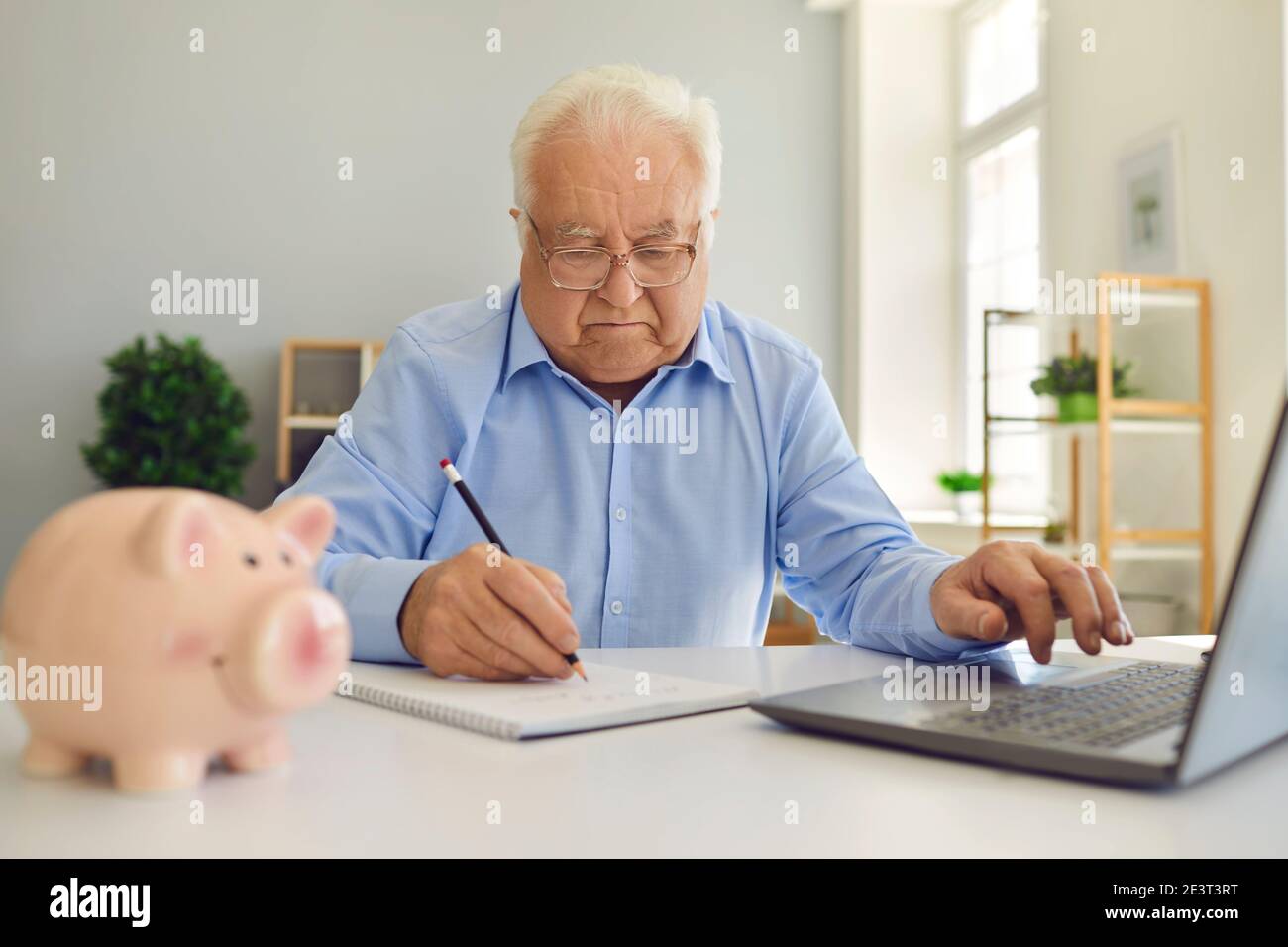 Uomo in pensione che usa un computer portatile e prende appunti durante lo studio di un notebook piano pensionistico e la gestione del suo bilancio Foto Stock