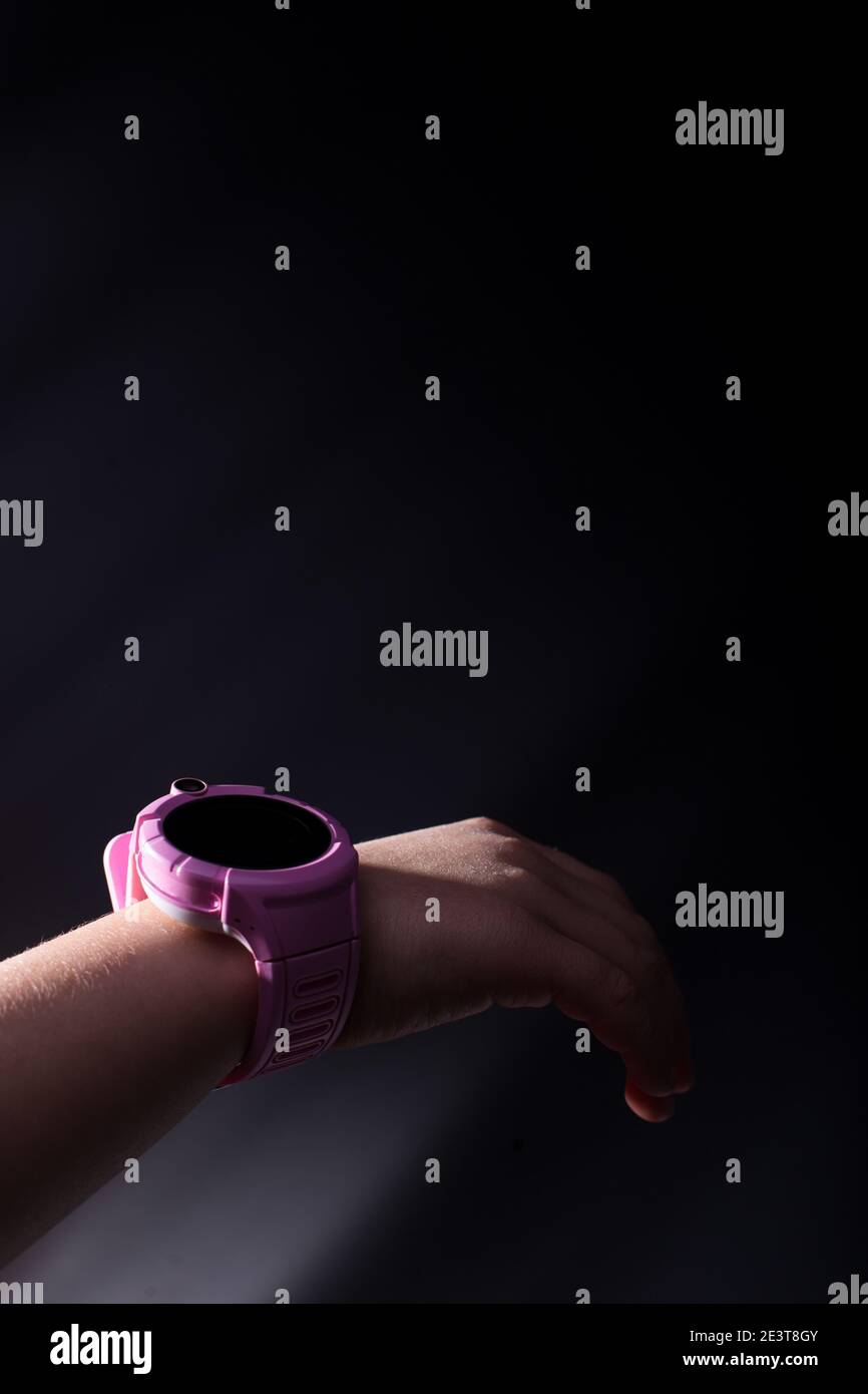 Orologio intelligente per bambini rosa a portata di mano su sfondo nero con copyspace. Foto Stock