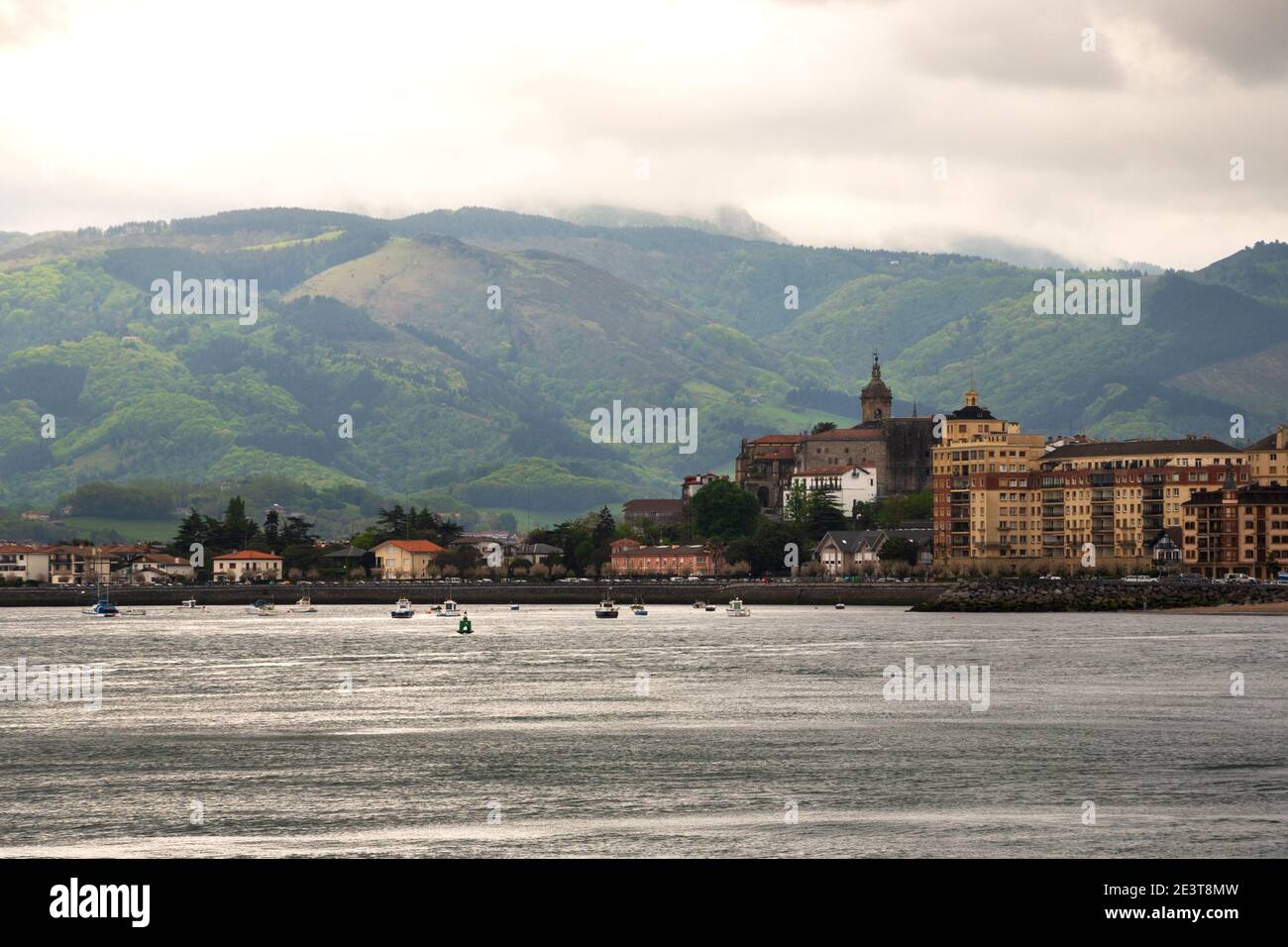Spagna. Vista del porto turistico di Hondarribia, degli edifici della città e della montagna di Jaizkibel sullo sfondo in nuvoloso giorno primaverile con illuminazione drammatica. Foto Stock