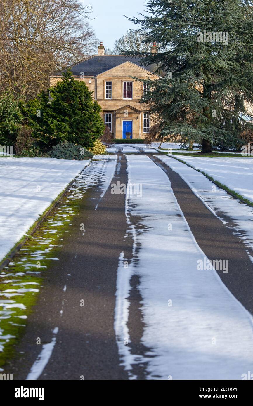 Un lungo e rettilineo percorso coperto di neve e giardino che conduce verso Una casa georgiana con una porta blu Foto Stock