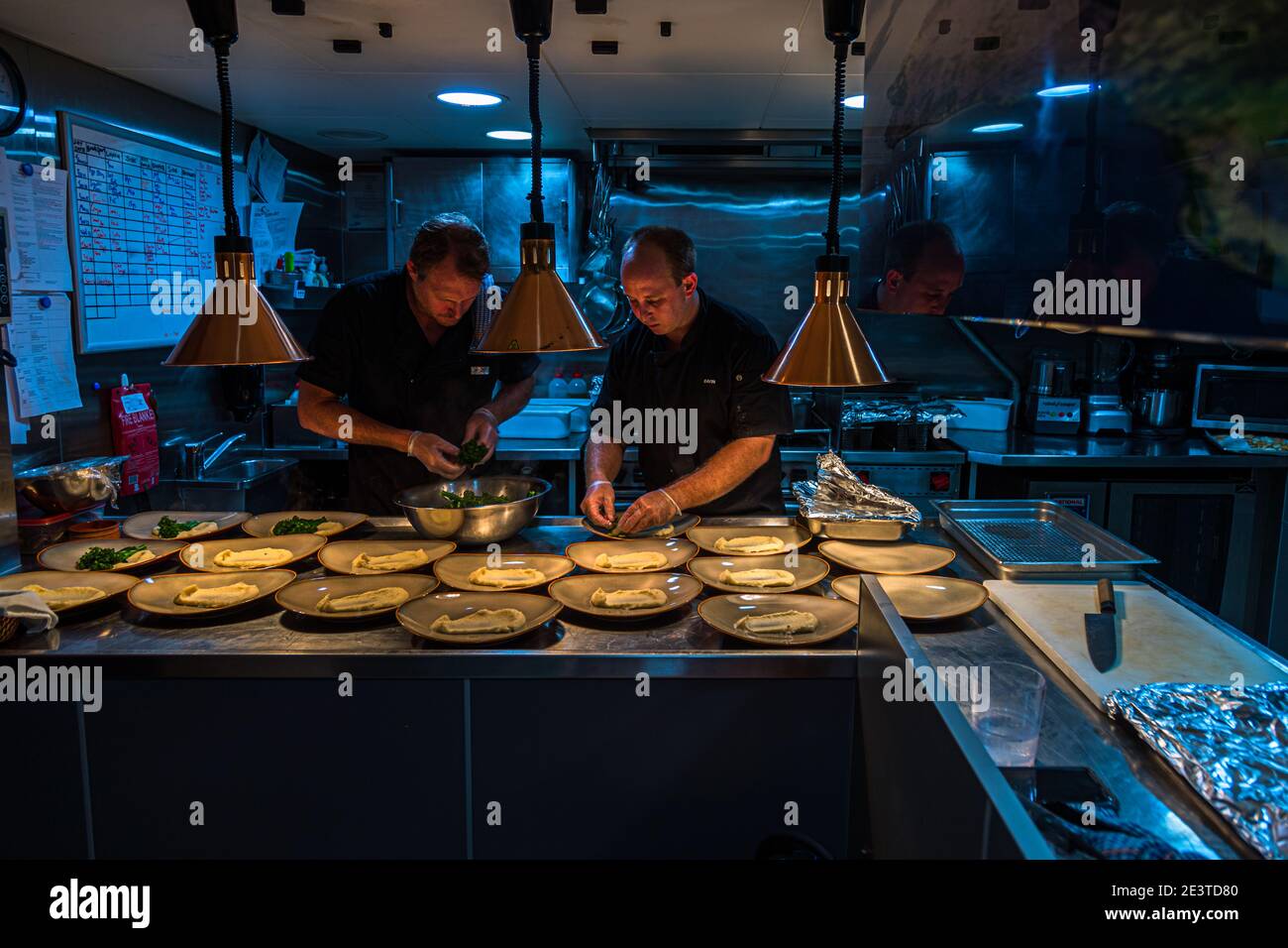 Due chef preparano gli antipasti nella cambusa della nave di spedizione True North, lampade termiche che illuminano la superficie di lavoro. Foto Stock