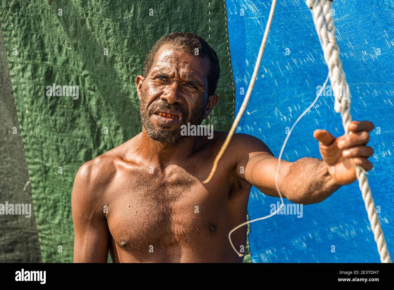 Lo skipper di una proa tiene una corda all'albero, i pannelli colorati della vela si estendono dietro di lui al largo della provincia di Milne Bay, Papua Nuova Guinea. Foto Stock
