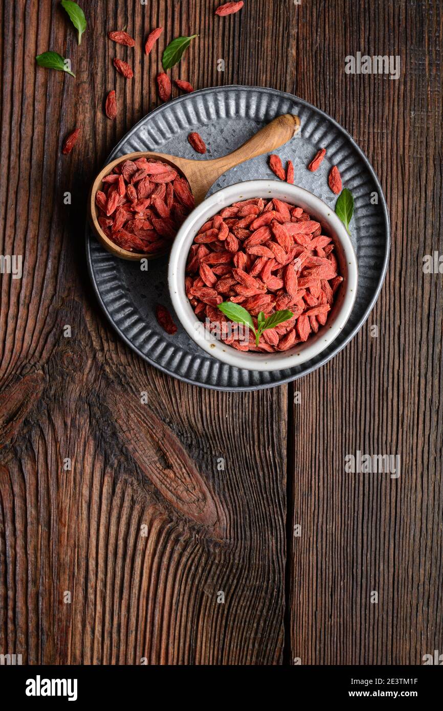 Snack sano ricco di antiossidanti e vitamine per aumentare l'immunità, bacca Goji essiccata in una ciotola e scoop su fondo rustico di legno con copia spac Foto Stock