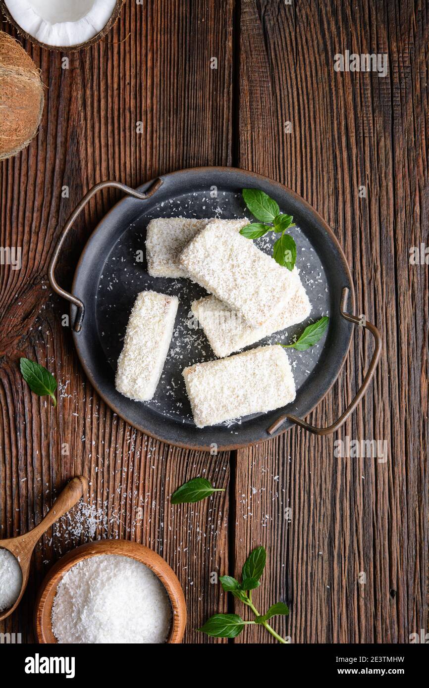 Delizioso dessert dolce, Lamingtons cioccolato bianco coperto di cocco grattugiato su rustico sfondo di legno Foto Stock