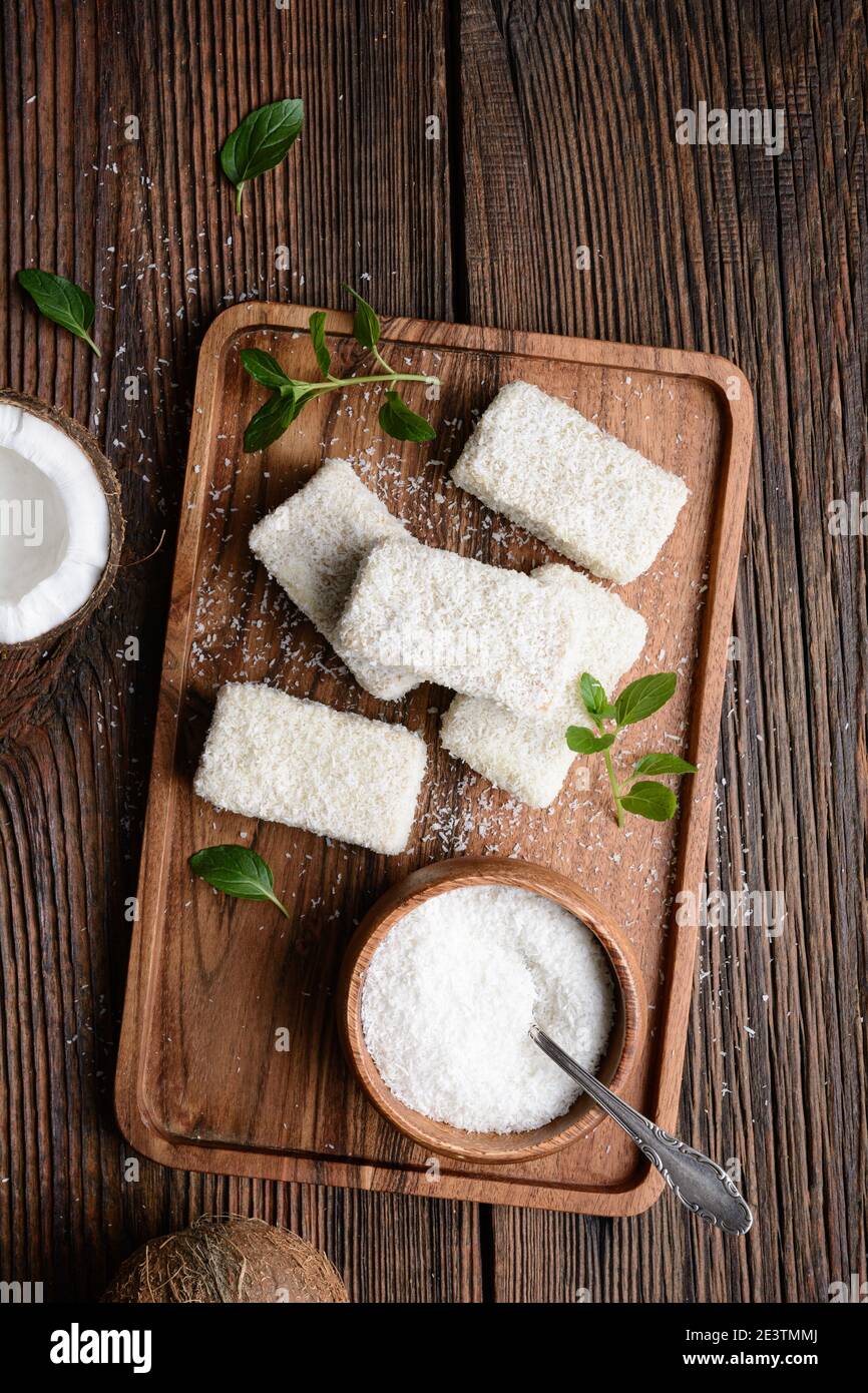 Delizioso dessert dolce, Lamingtons cioccolato bianco coperto di cocco grattugiato su rustico sfondo di legno Foto Stock