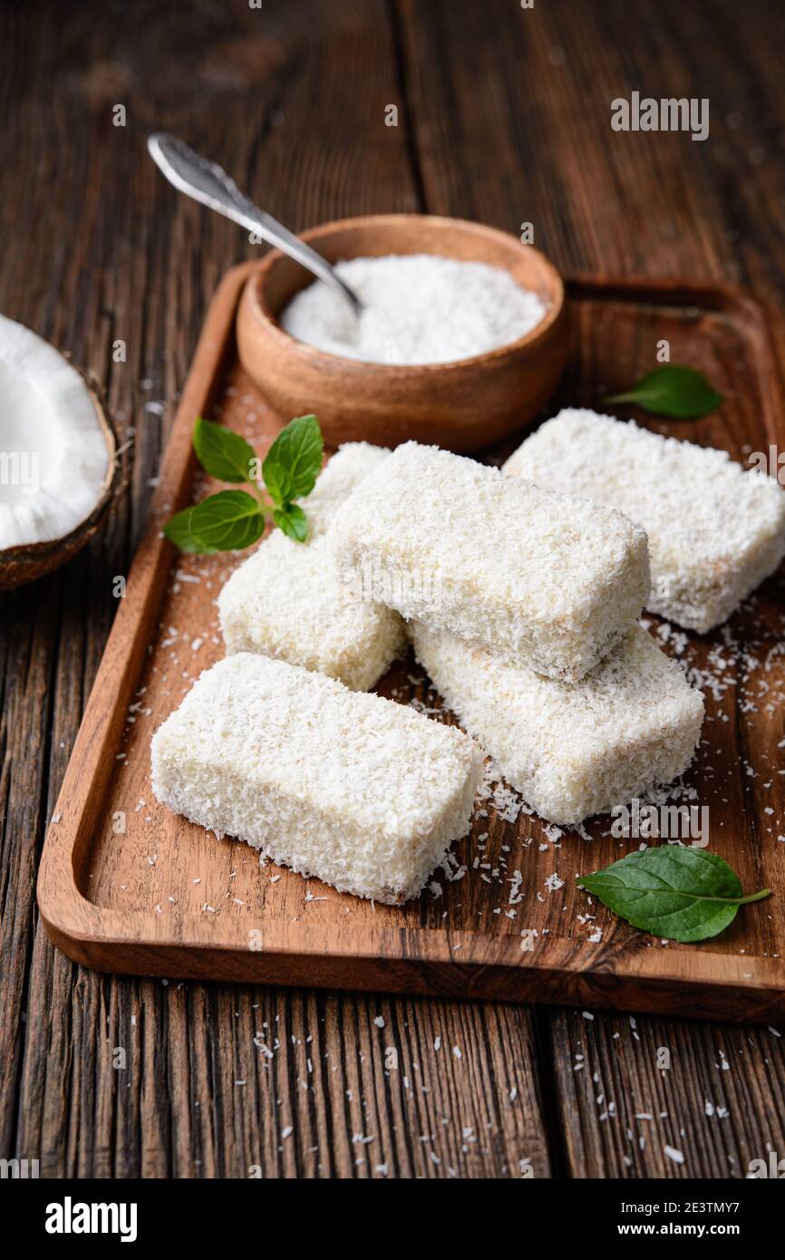 Delizioso dessert dolce, Lamingtons cioccolato bianco coperto di cocco grattugiato su rustico sfondo di legno Foto Stock