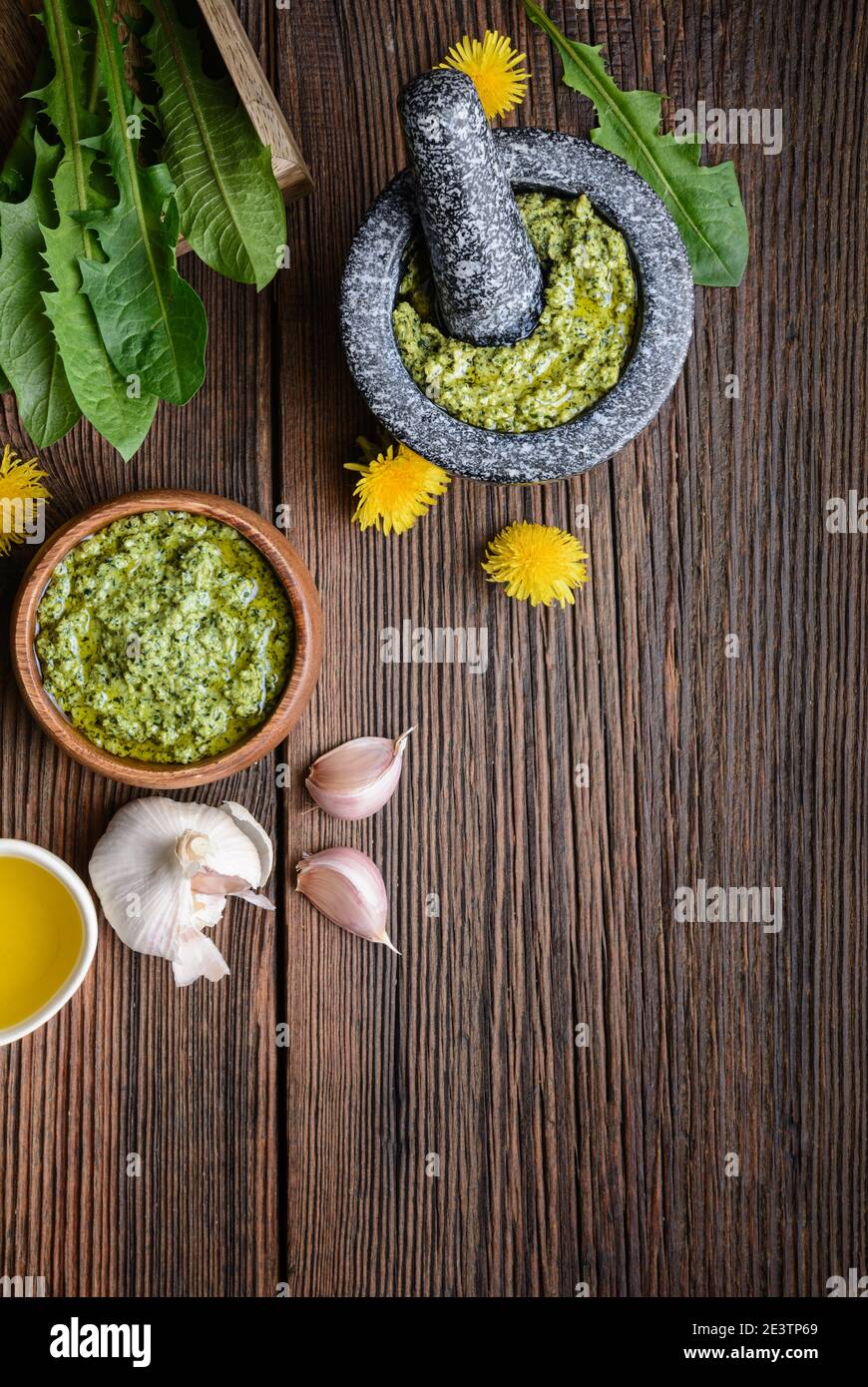 Sano pesto di dente di leone con mandorle, aglio, olio d'oliva e parmigiano in un mortaio di pietra su rustico sfondo di legno con spazio di copia Foto Stock