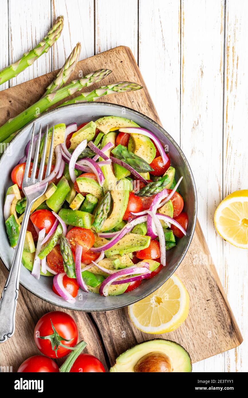Pasto vegano sano, insalata estiva Juicy con asparagi scottati, pomodori ciliegini, fette di avocado e cipolla rossa, cosparsa di pepe e condita con Foto Stock