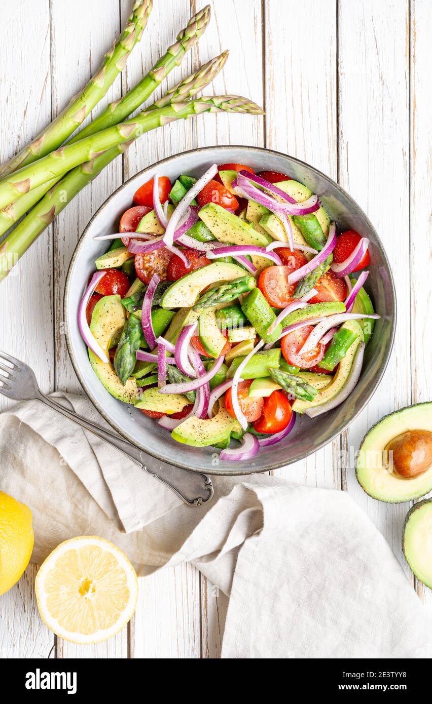 Pasto vegano sano, insalata estiva Juicy con asparagi scottati, pomodori ciliegini, fette di avocado e cipolla rossa, cosparsa di pepe e condita con Foto Stock