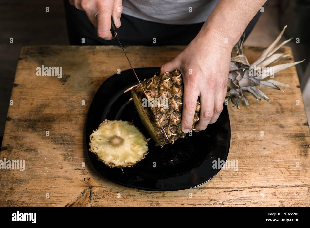 L'uomo taglia l'ananas con un coltello su un tavolo di legno Foto Stock
