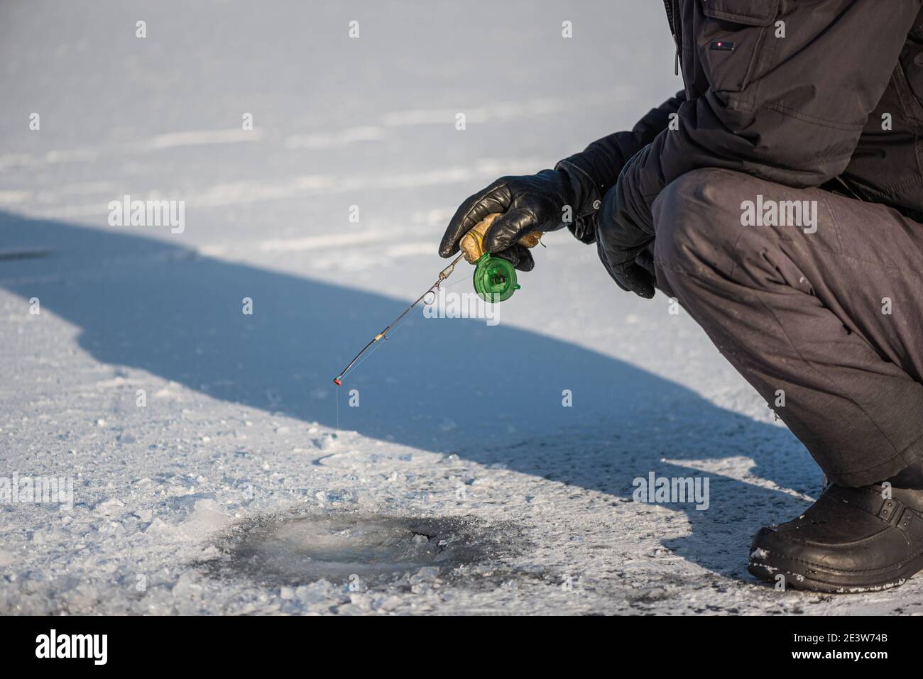 Pesca sul ghiaccio sul lago in giornata soleggiata gelata. Uomo seduto vicino al buco del ghiaccio che cattura il pesce. Attività invernale Foto Stock