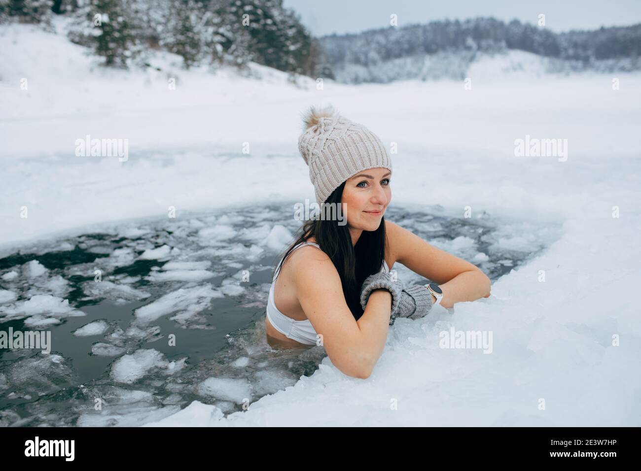 Nuoto invernale. Donna nel buco ghiacciato del lago. Come nuotare in acqua fredda. Bella giovane femmina sorridente. Cappelli e guanti per nuotare. Foto Stock