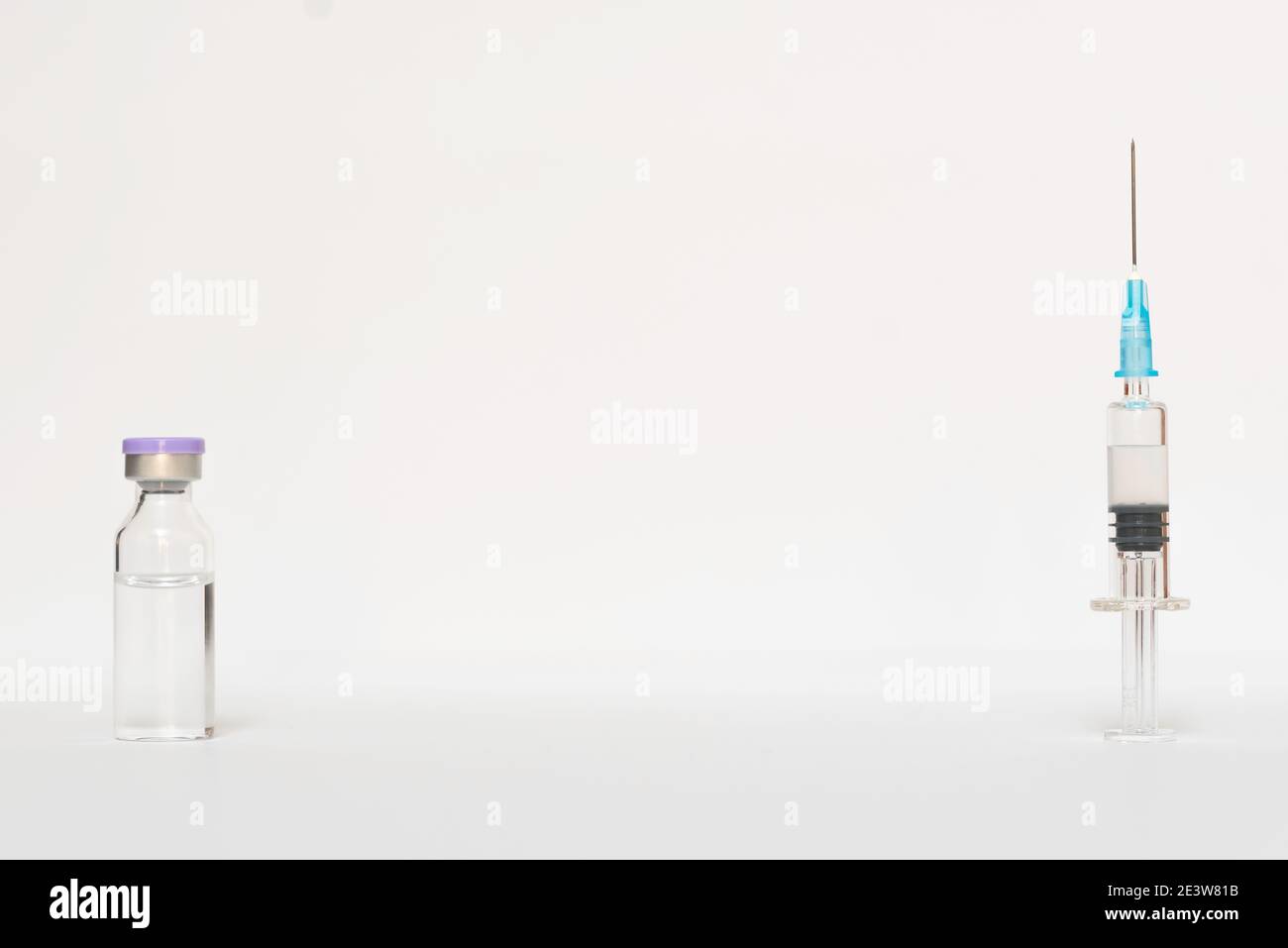 Sfondo bianco con un vaccino su un lato e il siringa con l'ago preparato sull'altro lato Foto Stock