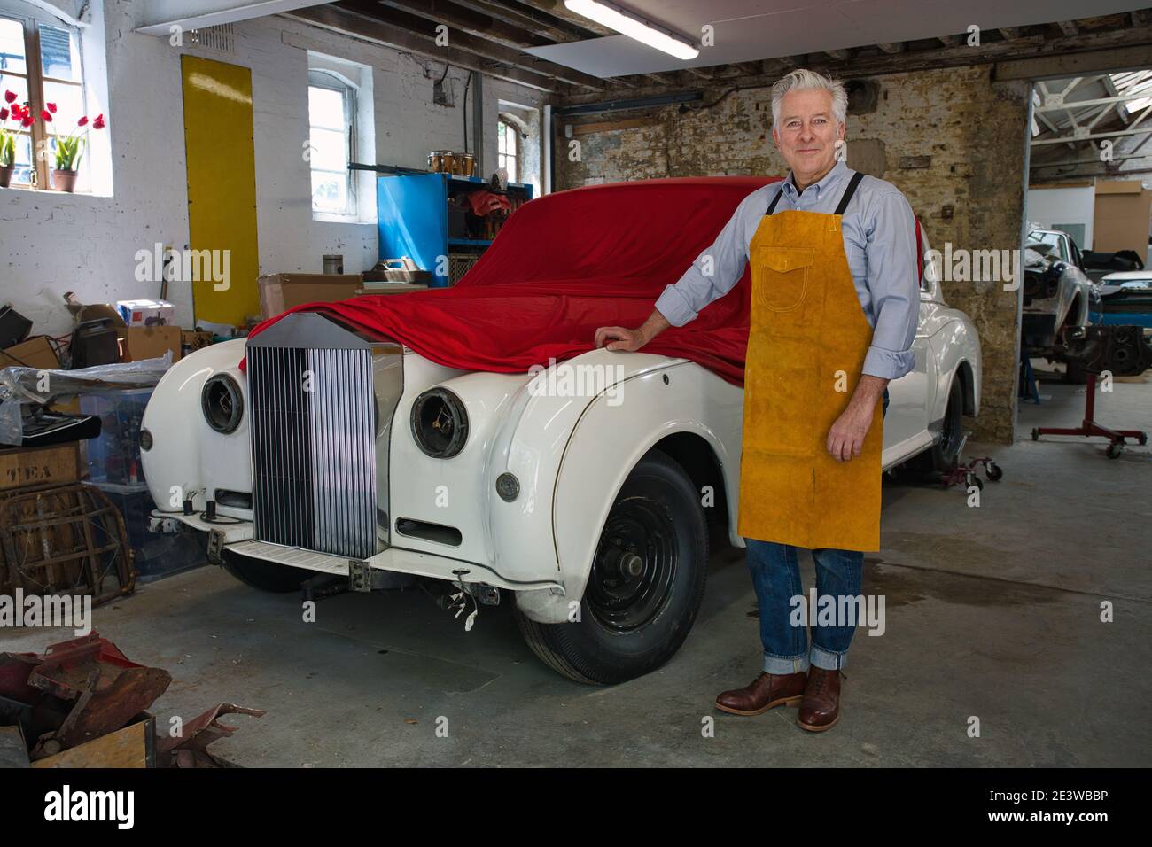 Orgoglioso meccanico in piedi accanto al coperto Rolls royce in un officina. Foto Stock