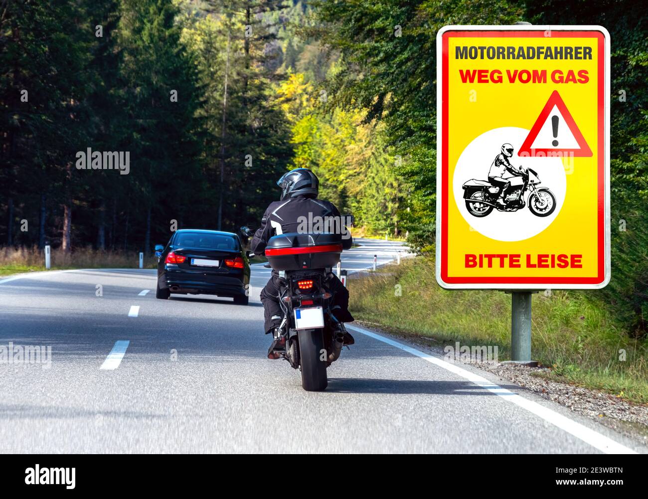 Scena di guida sulla strada con motociclista e segnaletica stradale 'Moto radfahrer weg vom gas -Bitte leise-' (motociclista fuori dal gas - si prega di fare silenzio) Foto Stock