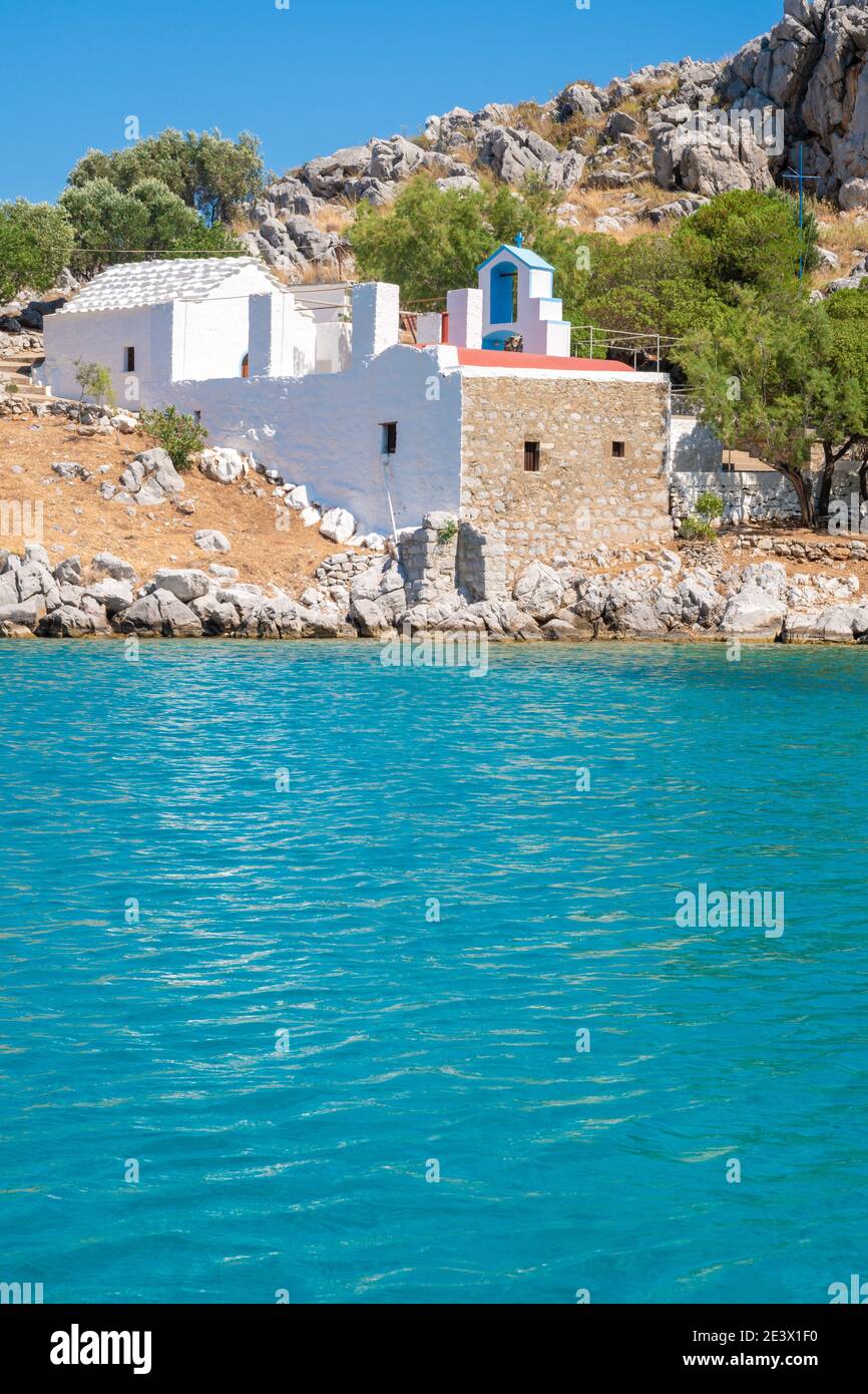 Vista dal mare in una baia con un edificio in pietra tra le rocce. Una chiesa greco-ortodossa in bianco e blu in armonia con la natura e il turchese Foto Stock