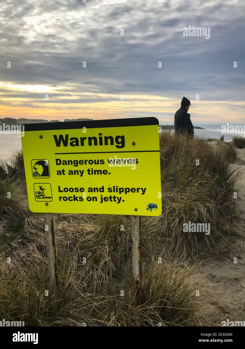 Segno giallo di avvertimento di onde pericolose e rocce scivolose. Immagine verticale. Foto Stock