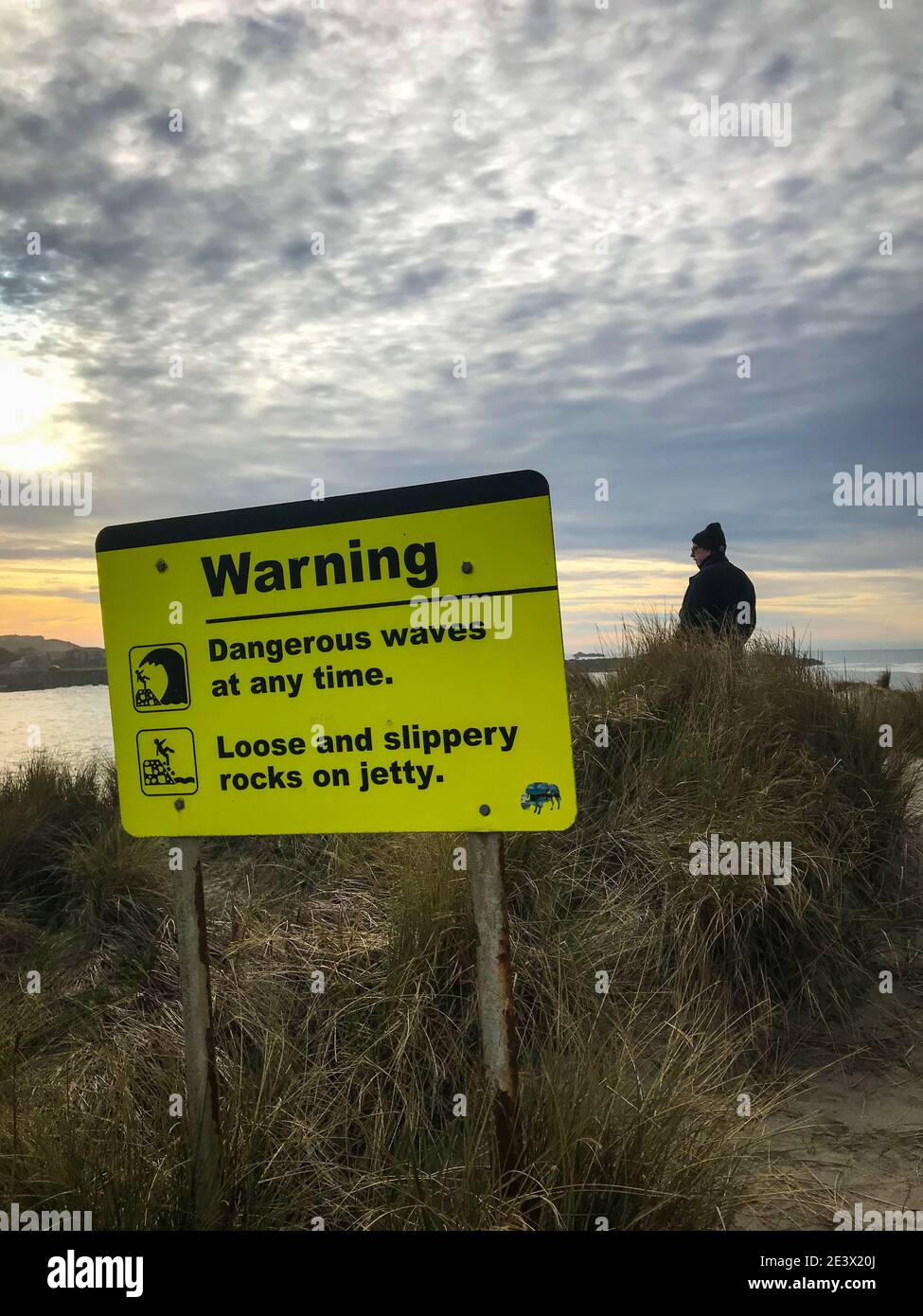Segno giallo di avvertimento di onde pericolose e rocce scivolose. Immagine verticale. Foto Stock