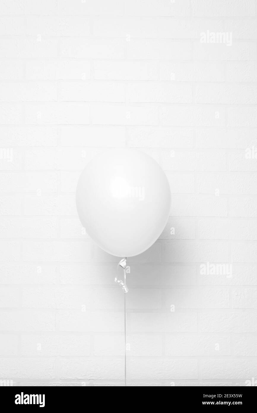 Palloncino di elio bianco su parete di mattoni bianchi. Formato verticale. Può essere usato come mock-up. Foto Stock