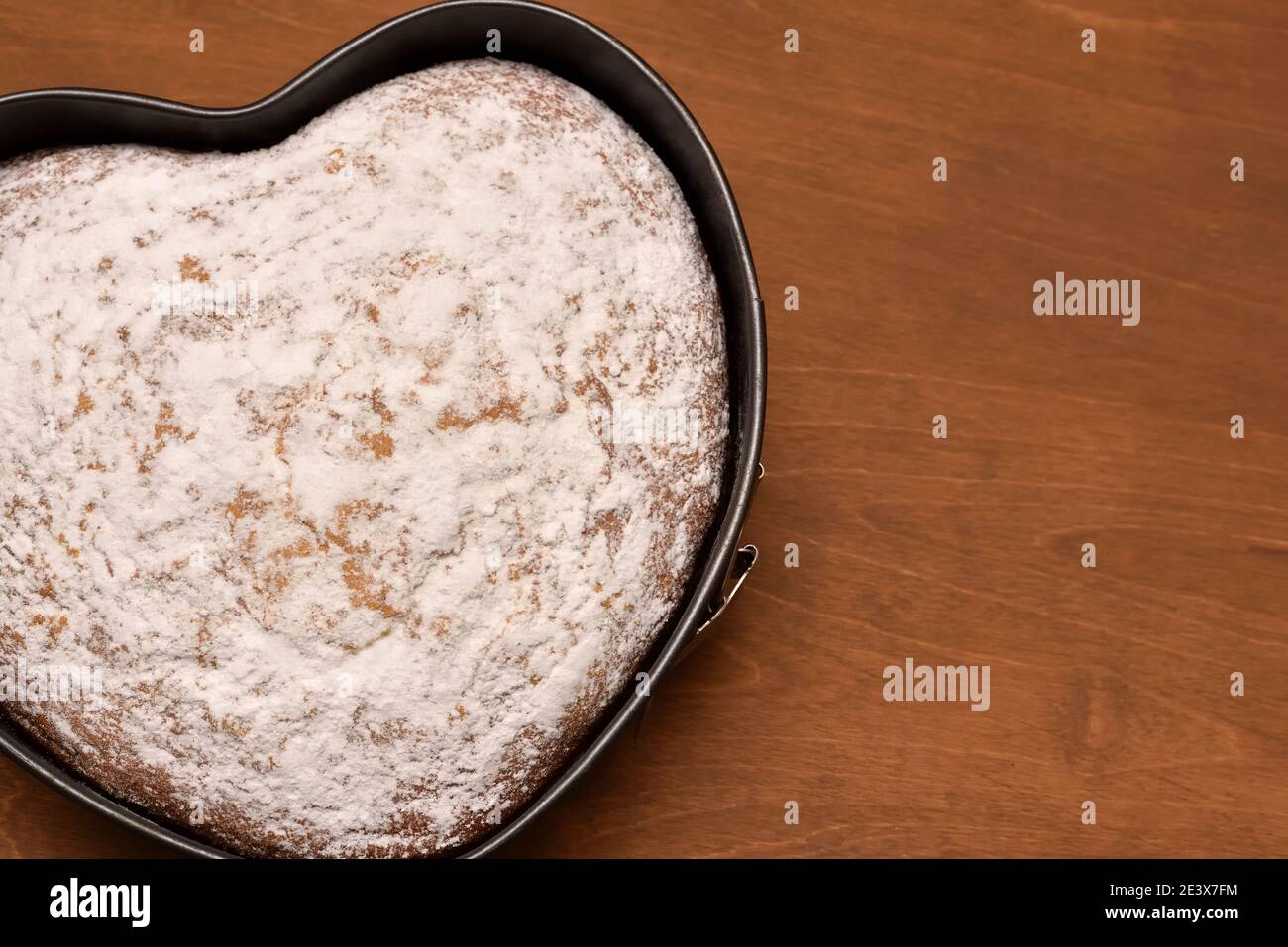 torta a forma di cuore in teglia primaverile, appena sfornata con amore e spolverata con zucchero in polvere Foto Stock