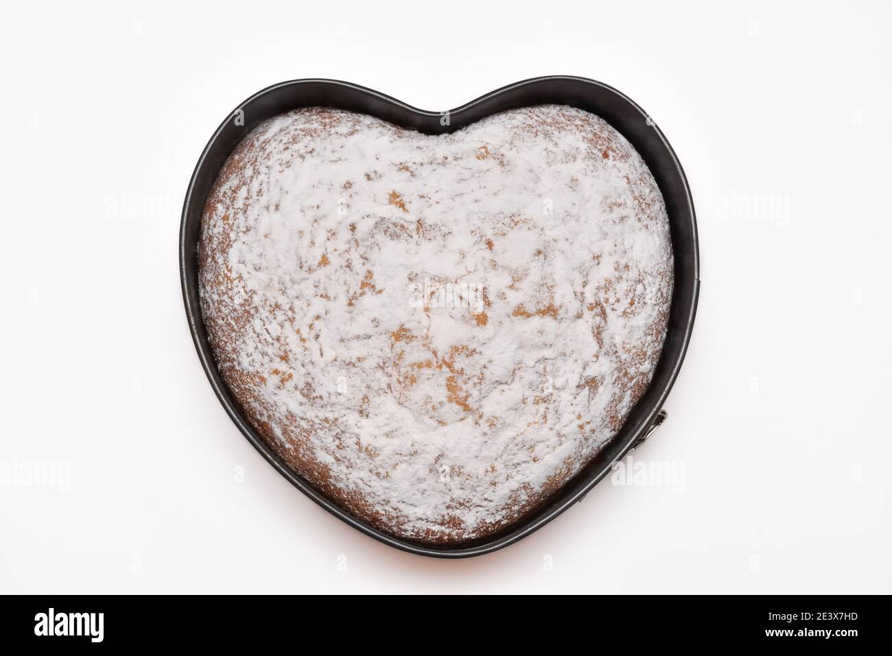 vista dall'alto della torta a forma di cuore appena sfornata in forma di molla tegola e spolverati con zucchero in polvere su fondo bianco Foto Stock