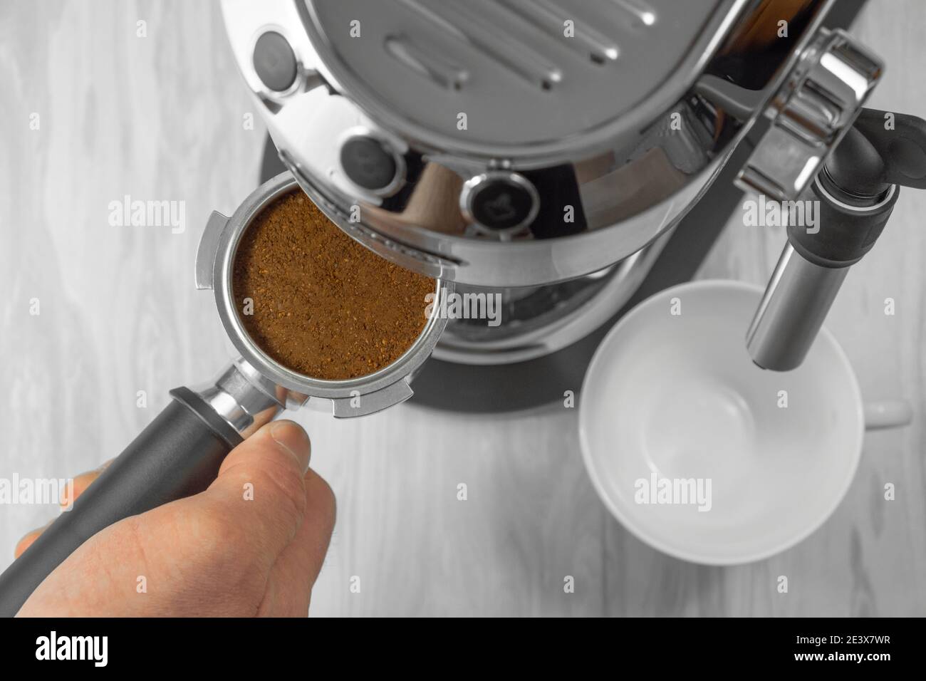 Il processo di preparazione di un espresso per una pausa caffè. Vista dall'alto di una mano che tiene un portafiltro di una macchina da caffè riempita di caffè macinato. Foto Stock