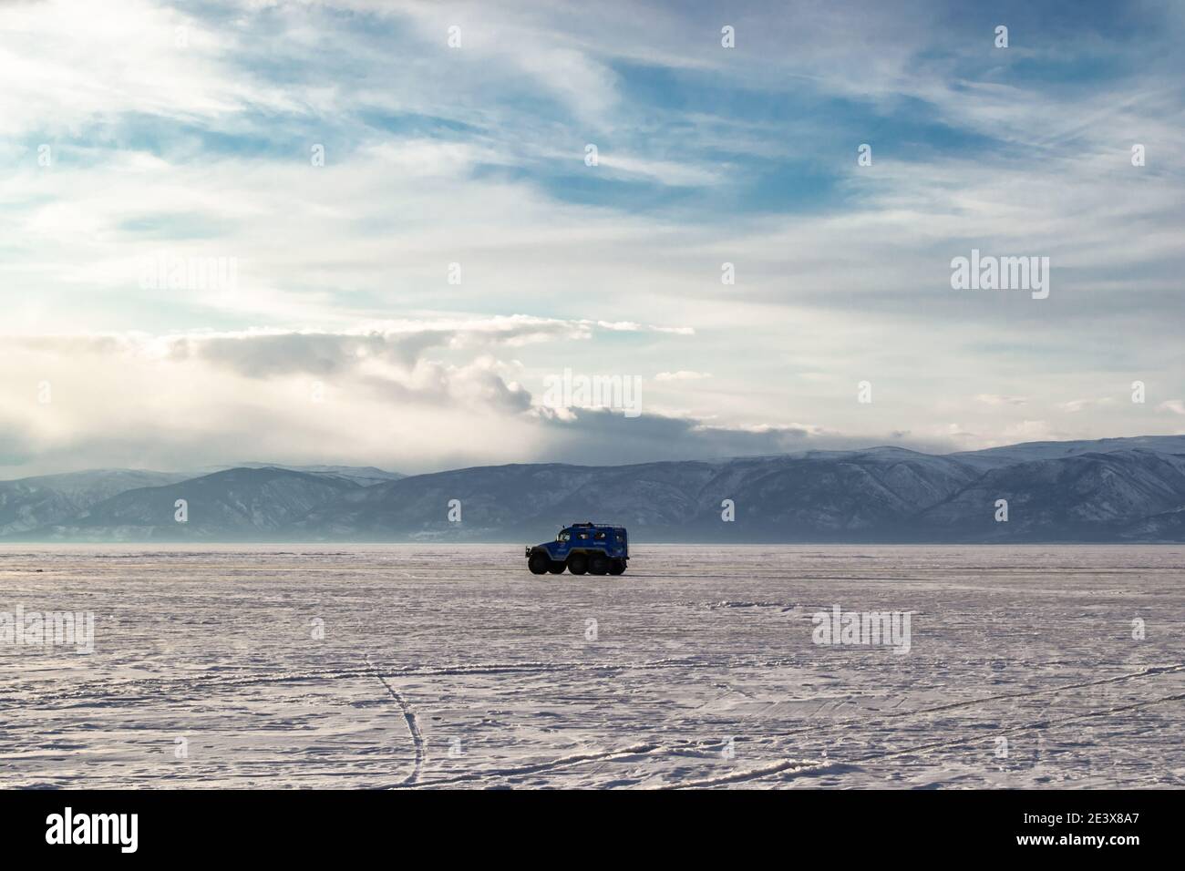 L'auto viaggia sul ghiaccio innevato del lago Baikal sullo sfondo delle montagne. Il concetto di guida fuoristrada in condizioni estreme. Foto Stock