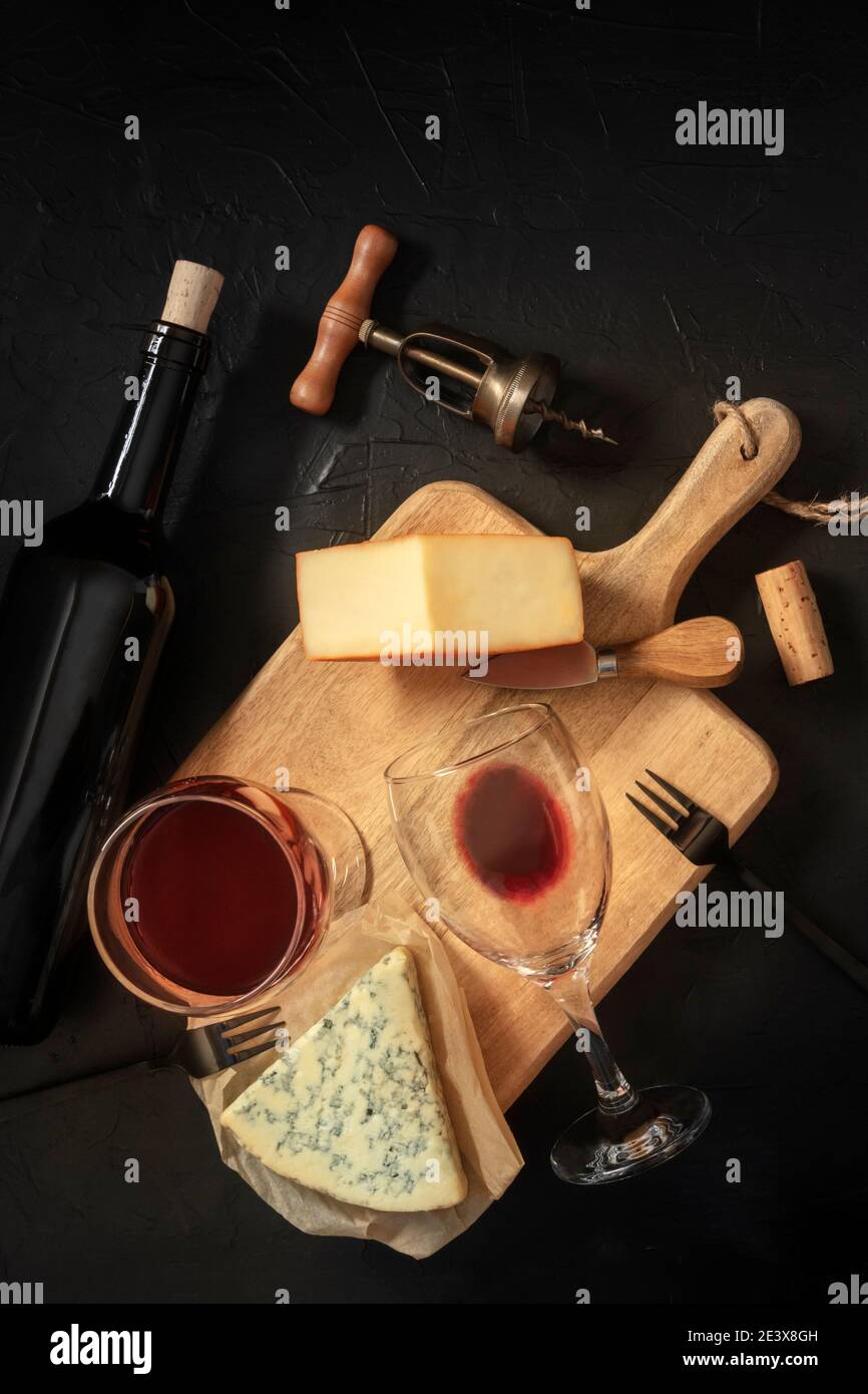 Degustazione di vini e formaggi, sparati dall'alto su sfondo nero, con un tappo di sughero, cavatappi d'annata e una bottiglia Foto Stock