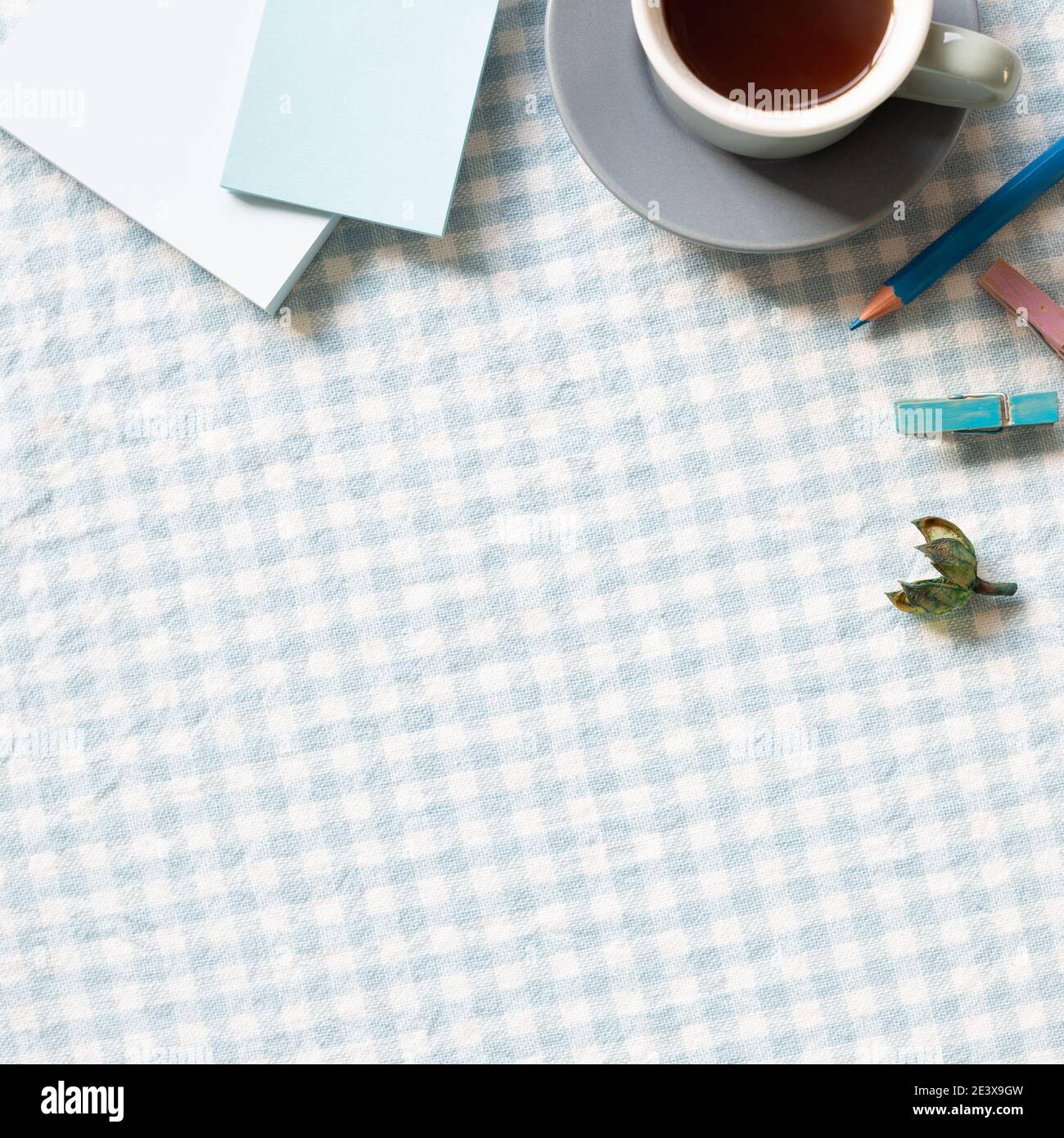 Luogo di lavoro e di studio. Tazza di caffè, blocco note, matita colorata, clip su sfondo di tessuto con motivo di controllo blu. Posa piatta, vista dall'alto, spazio per la copia Foto Stock