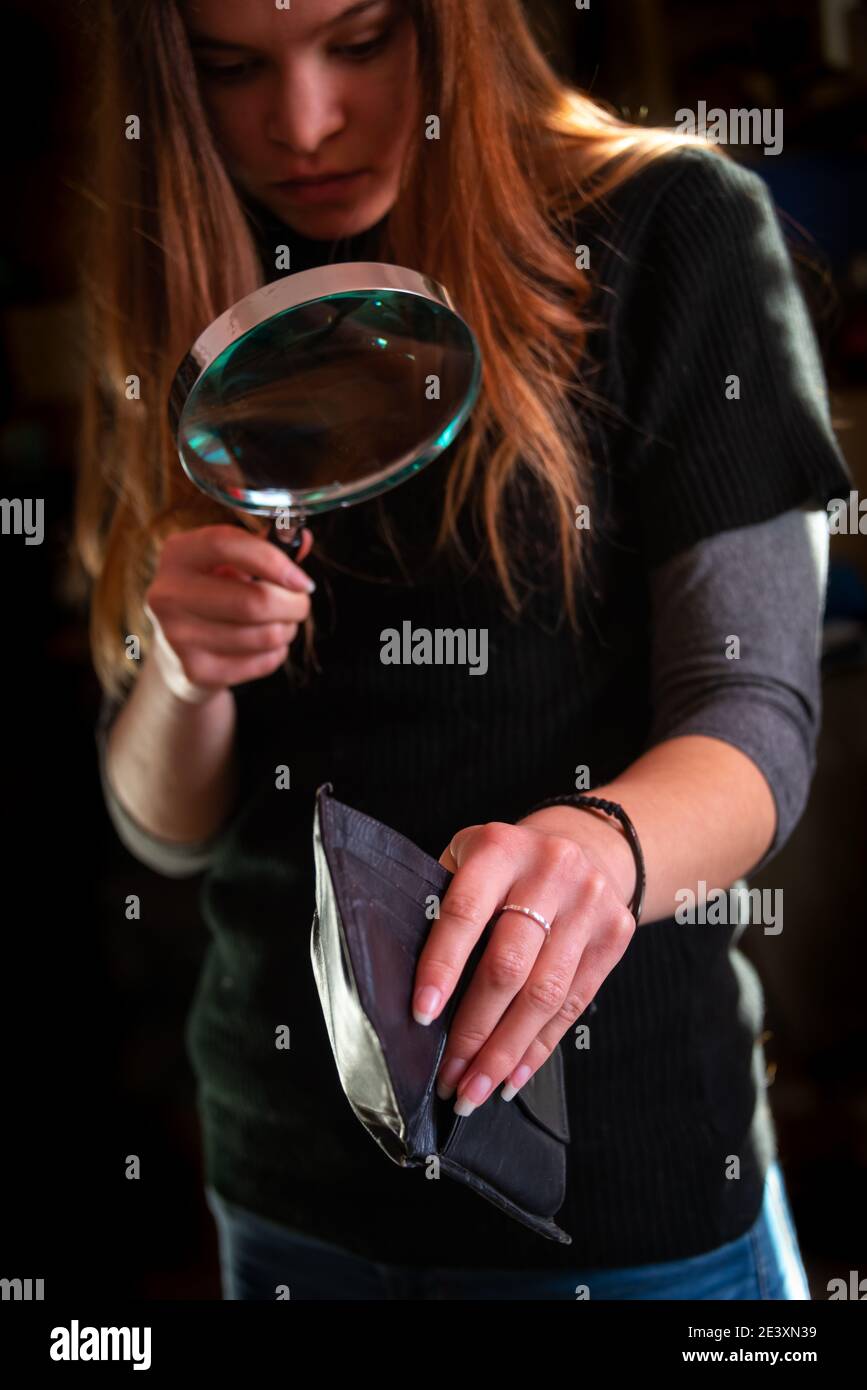 giovane donna che guarda in un portafoglio vuoto con lente d'ingrandimento,  costo della finanza domestica vivente Foto stock - Alamy