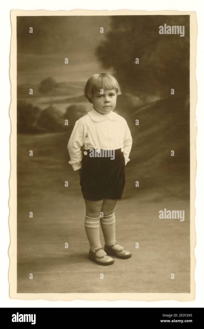 Originale primo 1900's studio ritratto foto di ragazzo di circa 3 anni con pettinatura bob, in piedi aspetto serio, Regno Unito circa 1925 Foto Stock