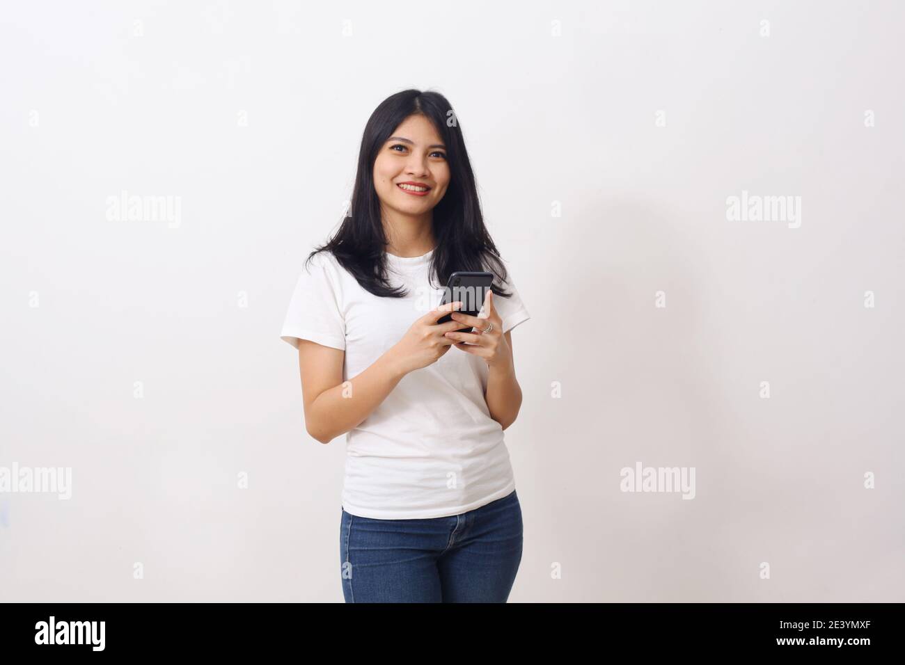 Ritratto di una ragazza asiatica felice che tiene il telefono cellulare e. guardando la telecamera isolata su sfondo bianco Foto Stock