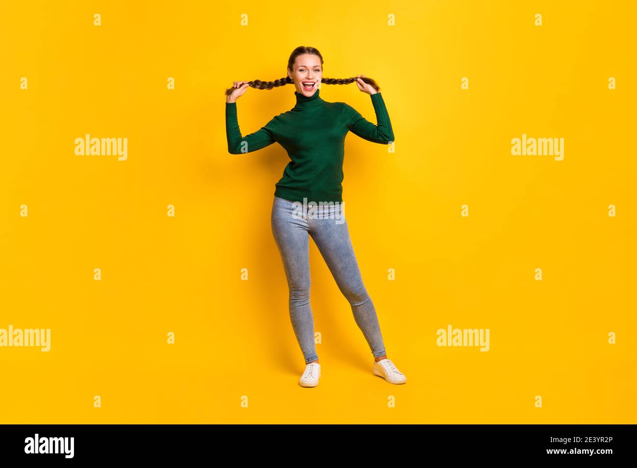 Foto ritratto a corpo intero di donna che tiene due code isolato su sfondo giallo brillante Foto Stock