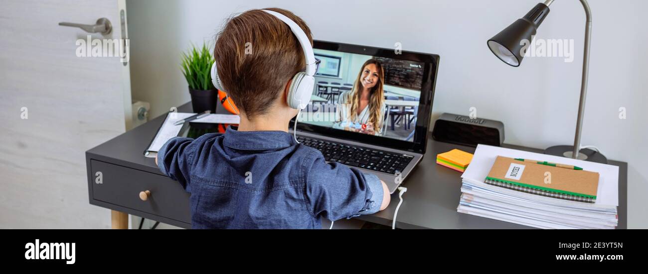 Ragazzo irriconoscibile con le cuffie che ricevono la classe a casa con il computer portatile dalla sua camera da letto. Concetto di scuola domestica Foto Stock