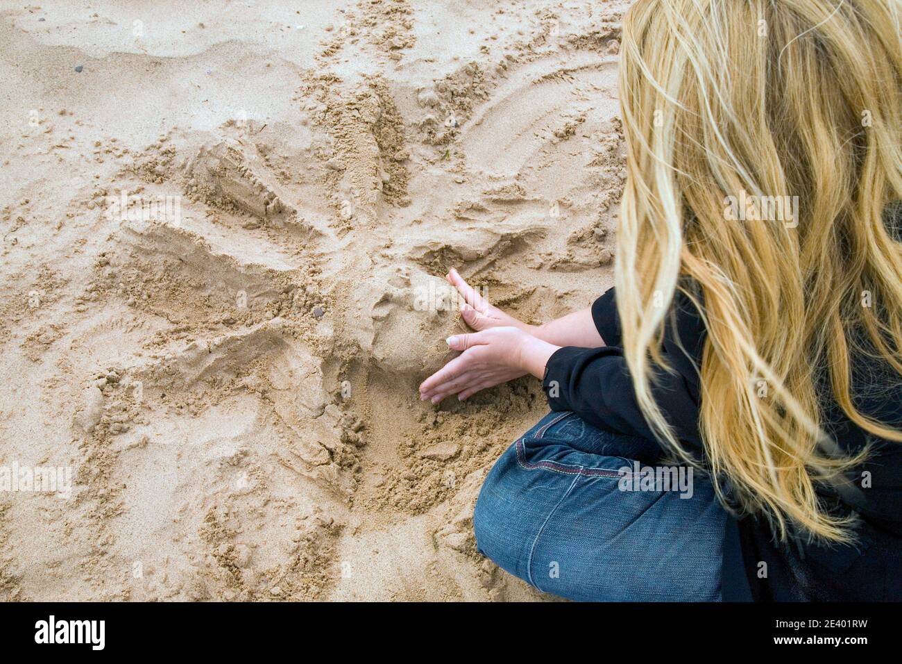 Lady che crea una maschera di sabbia ( The Green Man ) nella sabbia sulla spiaggia durante l'inverno, Exmouth, Devon, Inghilterra Foto Stock