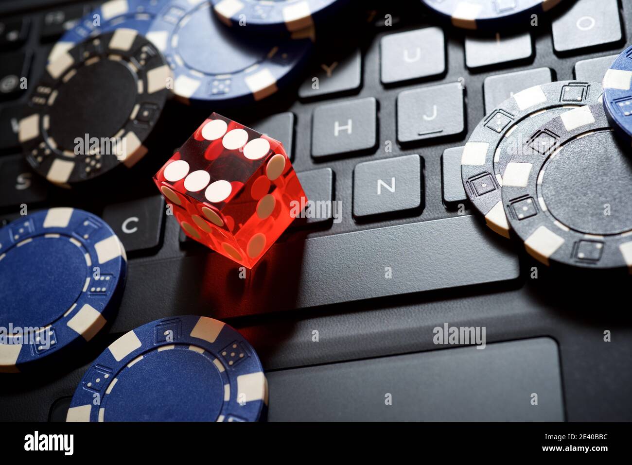 Casino chips e un dado rosso che si accatastano su un computer portatile. Foto Stock