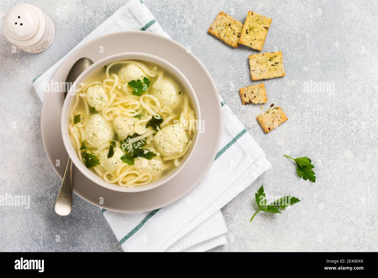 Ciotola di zuppa italiana tradizionale con polpette di pollo e pasta d'uovo, parmigiano, prezzemolo su sfondo grigio. Cucina italiana tradizionale. Foto Stock