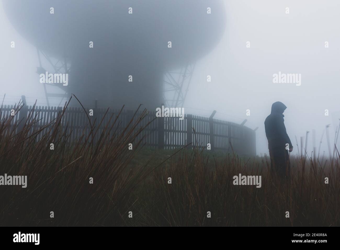 Guardando verso l'alto una figura agganciata in piedi accanto a a. stazione radar in un giorno foggy moody Foto Stock