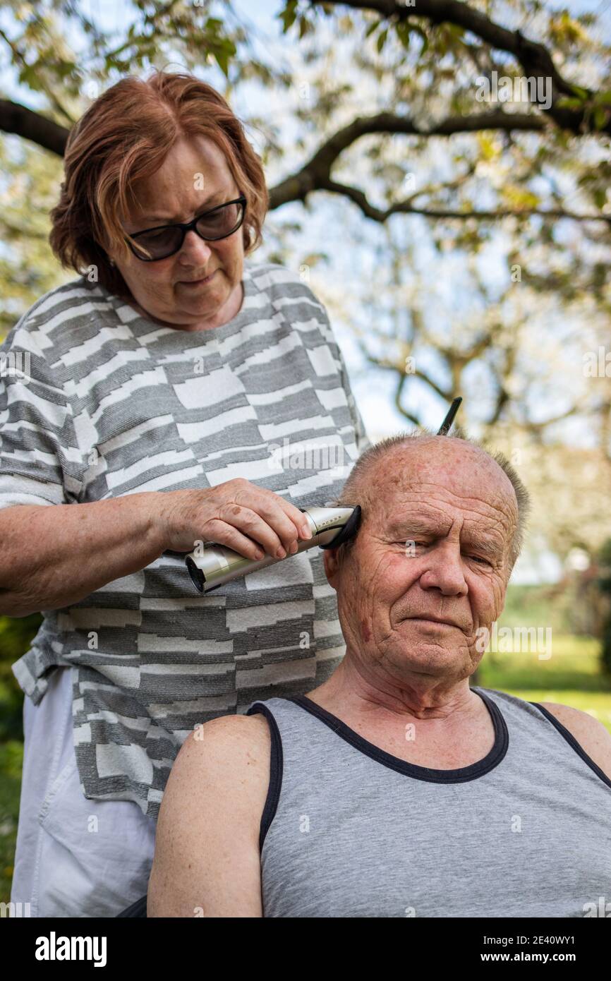 Rimani a casa, rimani sicuro e positivo e prenditi cura di te stesso all'interno della stessa famiglia durante il blocco del coronavirus. La coppia anziana sta facendo un taglio di capelli Foto Stock