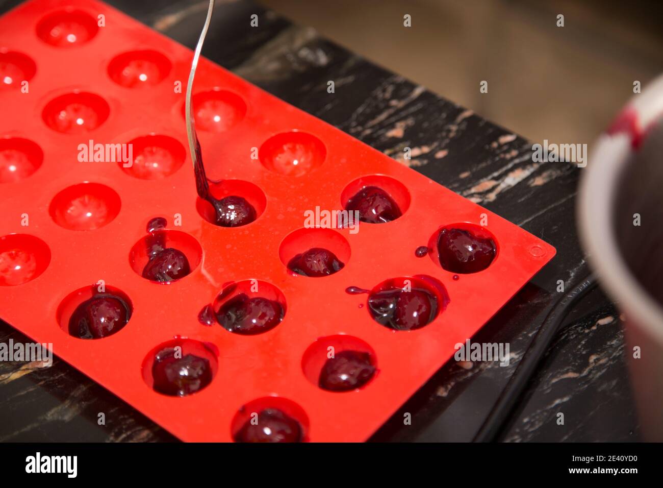 Apertura del riempimento in uno stampo in silicone. Il processo di produzione di cioccolatini con ripieno. Primo piano. Foto Stock