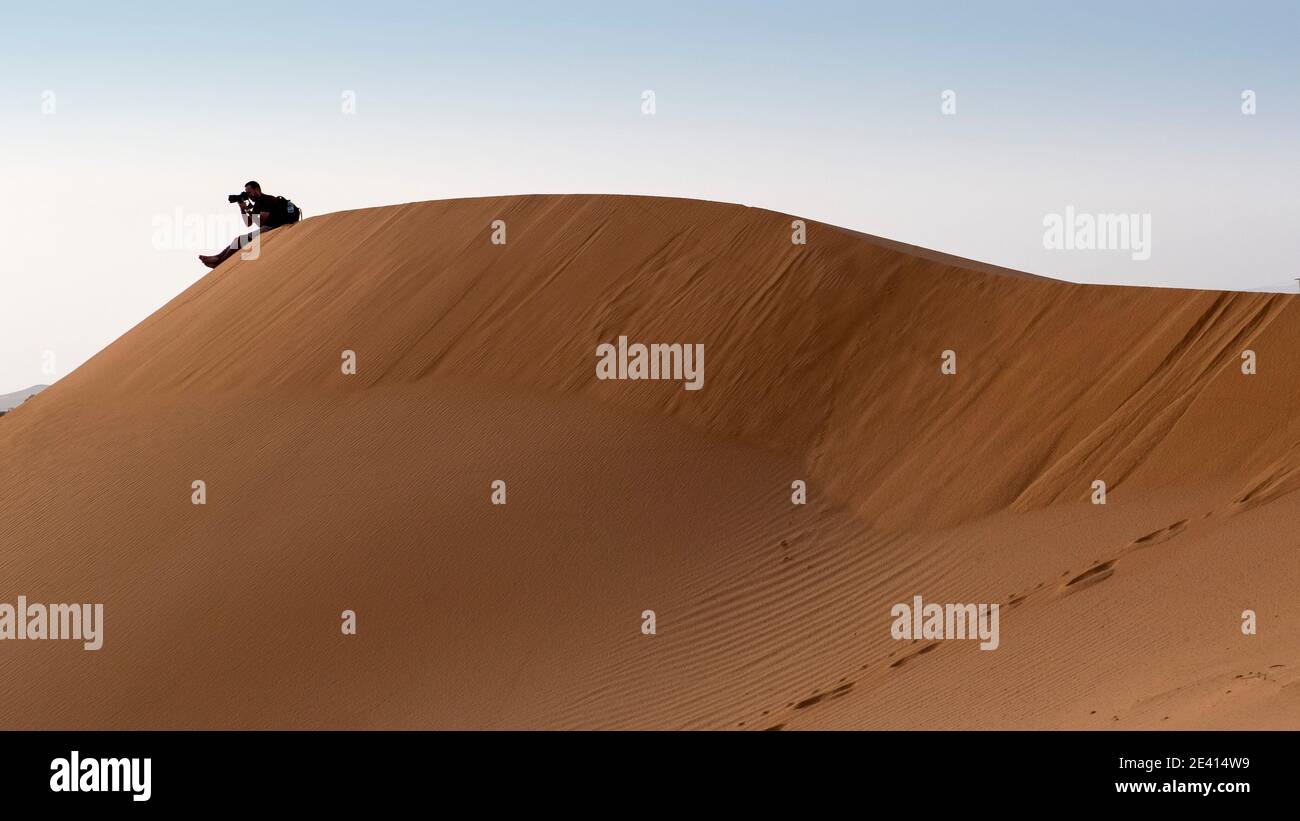 Un giovane che scatta foto con la sua fotocamera in cima a una duna nel deserto del Sahara in Marocco. Foto Stock