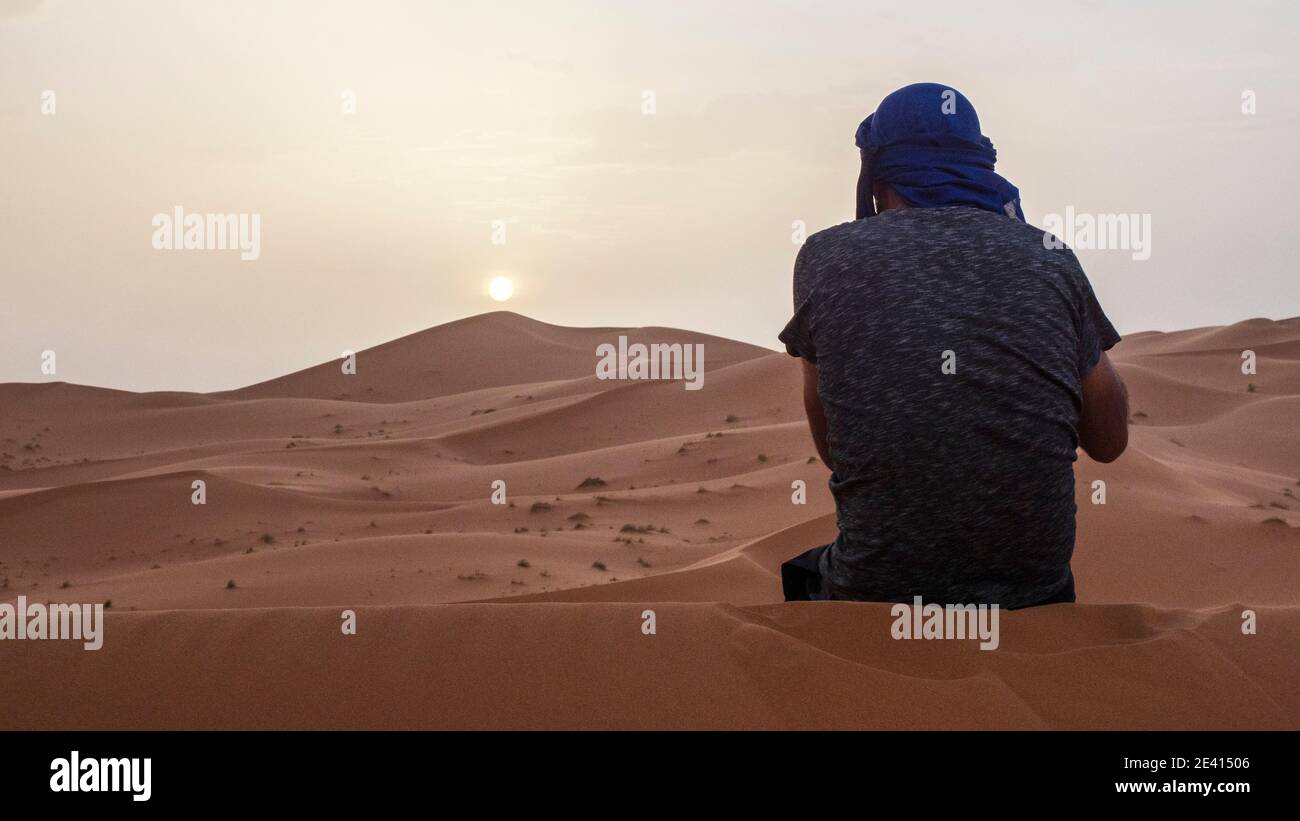Un giovane che scatta foto da una grande duna di sabbia nel deserto del Sahara del Marocco al tramonto. Foto Stock