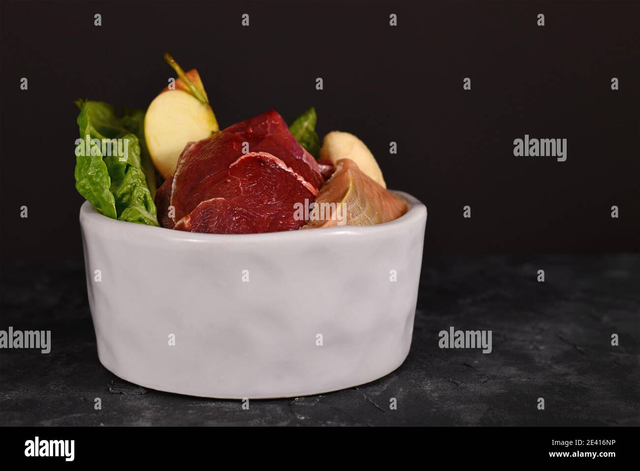 Ciotola del cane riempita con miscela di alimento crudo biologicamente appropriato contenente pezzi di carne, pesce, frutta e verdure su scuro Foto Stock